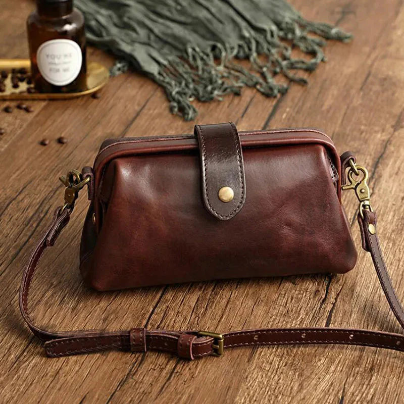Braune Ledertasche mit Schnalle und verstellbarem Schulterriemen auf Holztisch, Vintage-Stil, ideal für Damenmode und Accessoires.