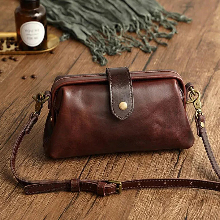 Braune Ledertasche mit Schnalle und verstellbarem Schulterriemen auf Holztisch, Vintage-Stil, ideal für Damenmode und Accessoires.