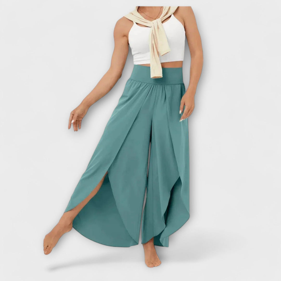 Frau in weißem Crop-Top und türkisfarbenen, weiten Hosen mit Schlitz. Modetrend, Sommeroutfit, lässiger Stil, Damenbekleidung.