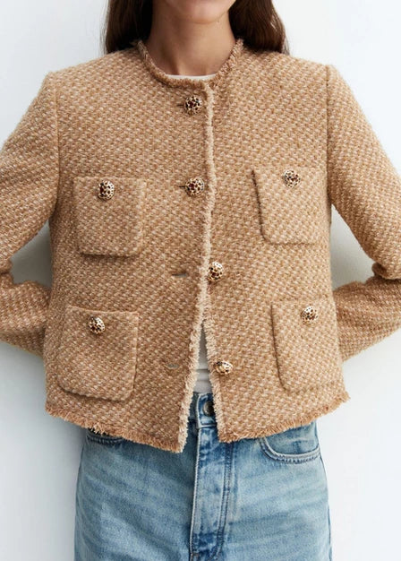 Frau trägt beige Bouclé-Jacke mit Knöpfen und Taschen, kombiniert mit blauer Jeans. Modetrend, elegante Damenmode, Herbstoutfit.
