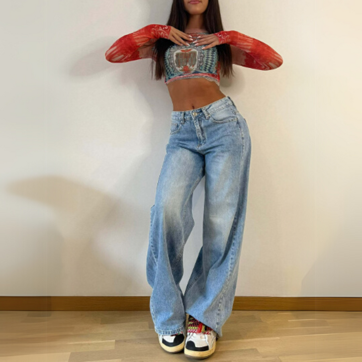 Frau in modischem Outfit mit rotem Langarm-Top, bauchfreiem Oberteil und weiten Jeans. Trendige Sneaker, lässiger Streetstyle-Look.