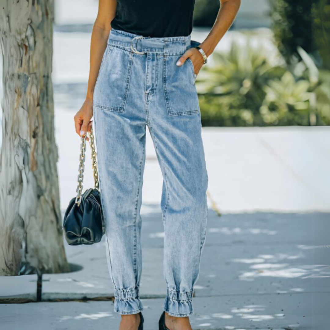 Frau in hochtaillierter, hellblauer Jeans mit Gürtel, schwarzem Oberteil und schwarzer Handtasche. Modetrend, lässiger Streetstyle, Sommermode.