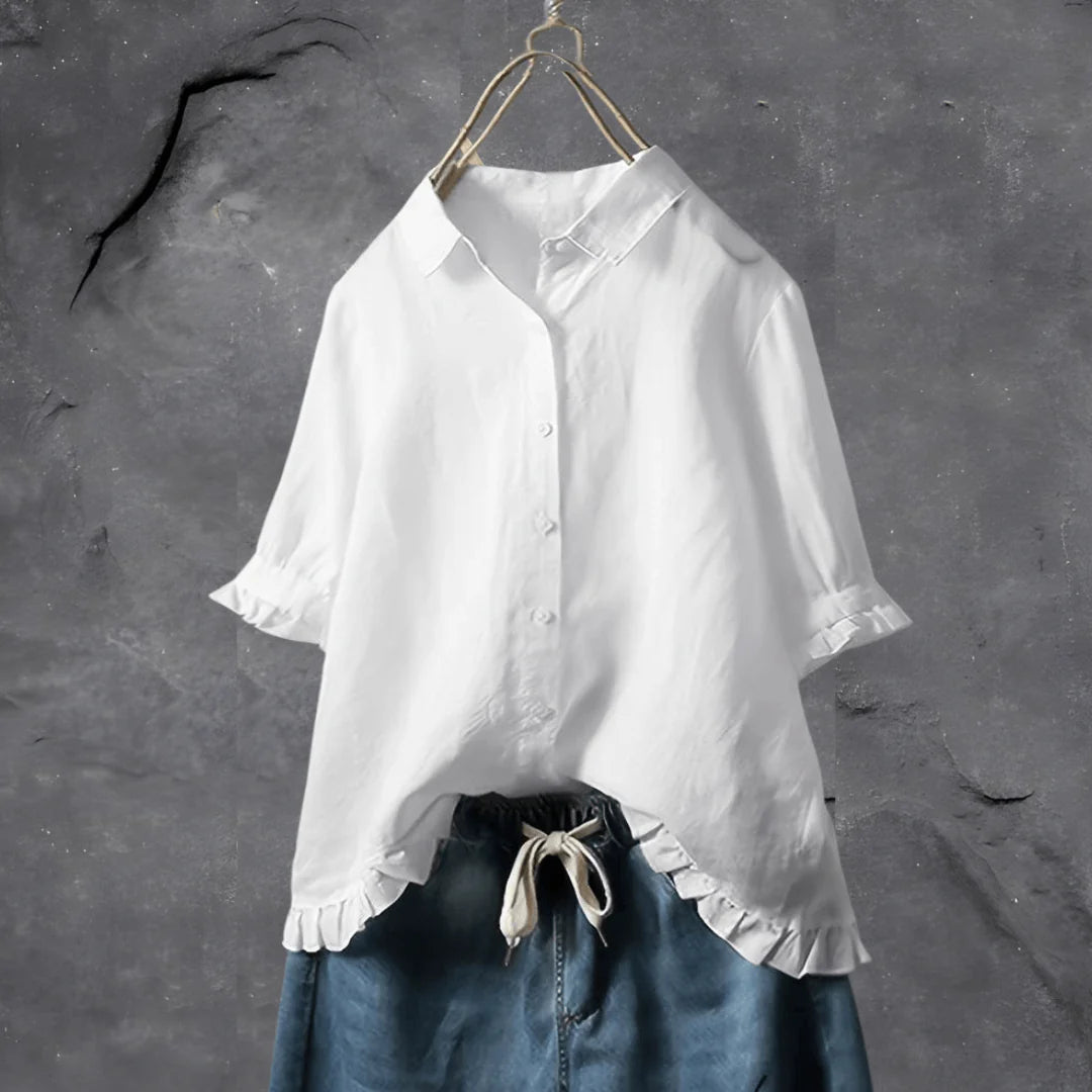 Weiße Bluse mit Rüschenärmeln auf einem Kleiderbügel vor grauem Hintergrund, kombiniert mit blauer Jeans. Modetrend, Damenbekleidung, stilvolle Outfits.