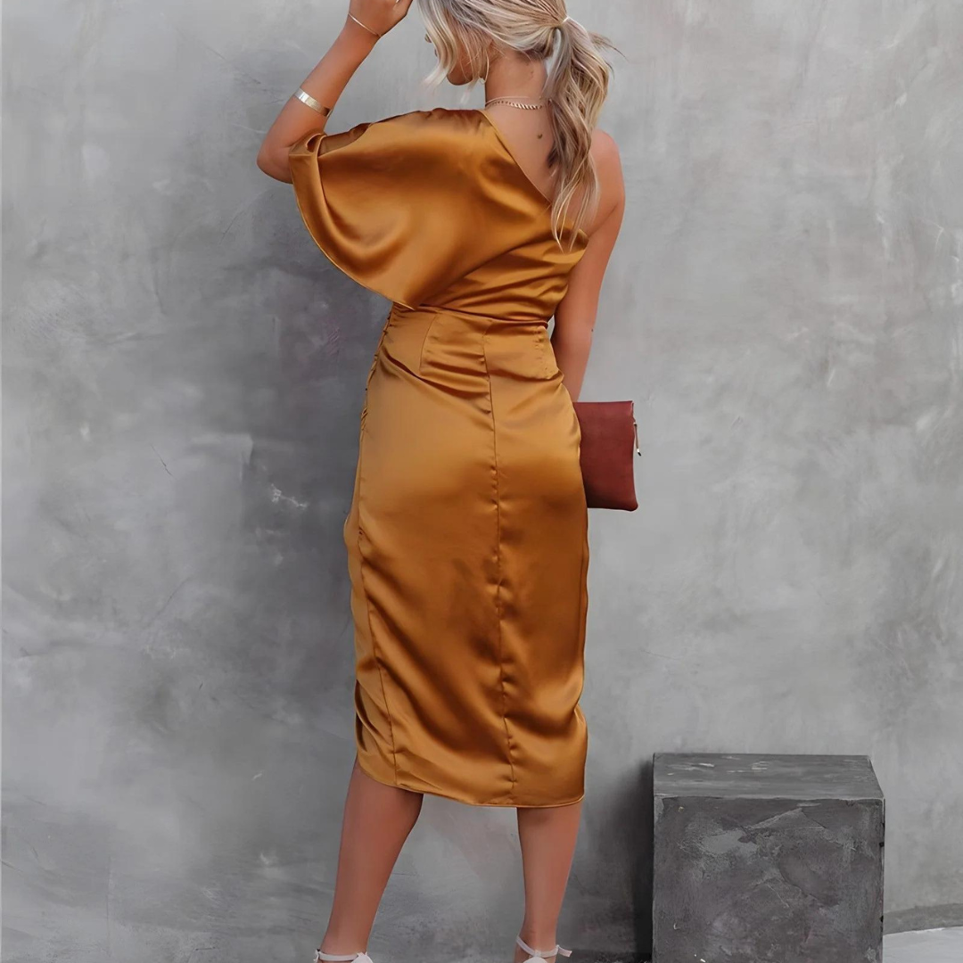 Frau in eleganten, goldenen Satin-Kleid, von hinten fotografiert, mit Clutch und Absatzschuhen, vor grauer Wand. Fashion, Abendmode, Damenkleidung.
