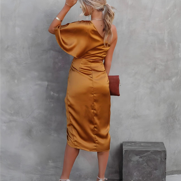 Frau in eleganten, goldenen Satin-Kleid, von hinten fotografiert, mit Clutch und Absatzschuhen, vor grauer Wand. Fashion, Abendmode, Damenkleidung.