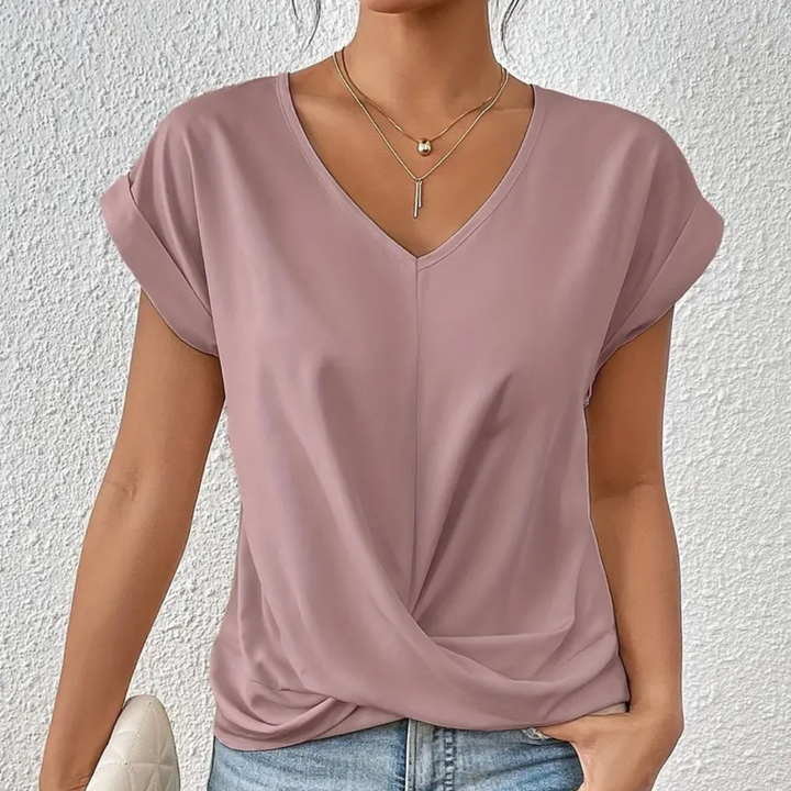Frau trägt lila V-Ausschnitt-Bluse mit Knoten-Detail, kombiniert mit blauen Jeans. Modetrend, Damenbekleidung, lässiger Stil.