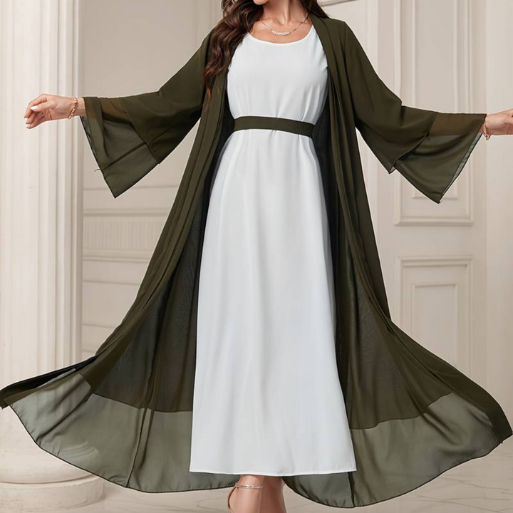 Frau in elegantem, langem, weißem Kleid mit olivgrünem Kimono in luxuriösem Innenraum. Mode, Abendkleid, stilvolle Damenbekleidung.