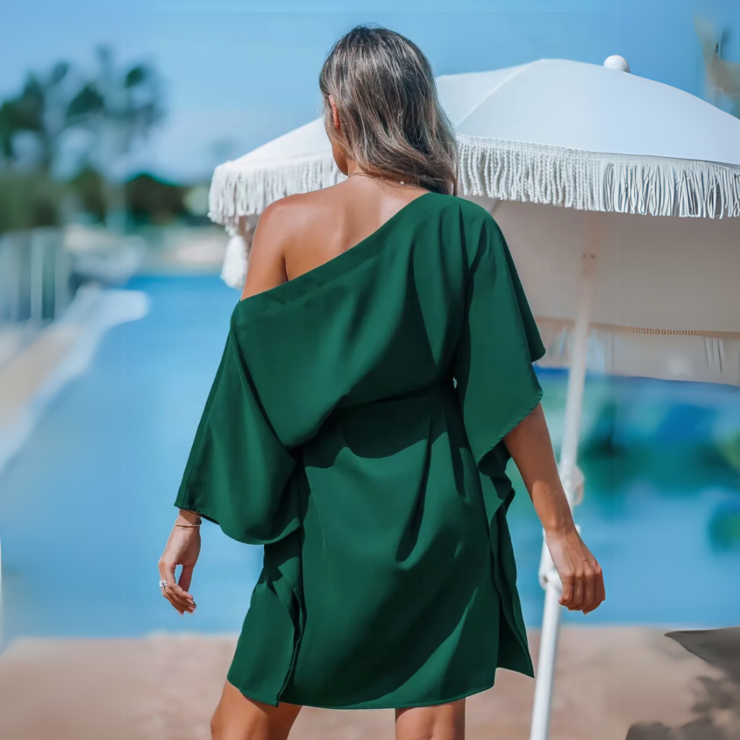Frau in grünem Sommerkleid am Pool, steht unter weißem Sonnenschirm. Sommermode, Urlaub, Entspannung, stilvolle Freizeitkleidung.