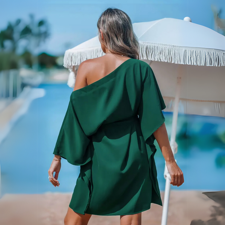 Frau in grünem Sommerkleid am Pool, steht unter weißem Sonnenschirm. Sommermode, Urlaub, Entspannung, stilvolle Freizeitkleidung.