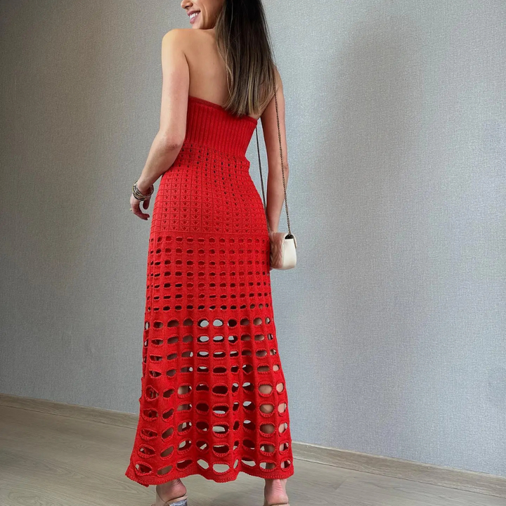 Frau in rotem, schulterfreiem Häkelkleid, steht vor grauer Wand. Elegantes Sommeroutfit, modisch, stilvoll, mit weißer Handtasche.