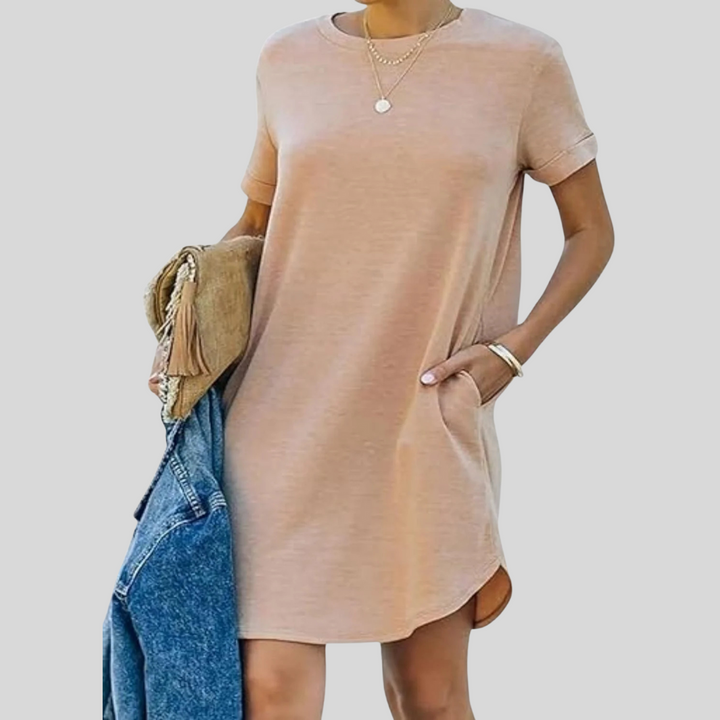 Frau in beigem T-Shirt-Kleid mit kurzen Ärmeln, hält blaue Jeansjacke und braune Tasche. Modetrend, lässiger Stil, Damenmode.