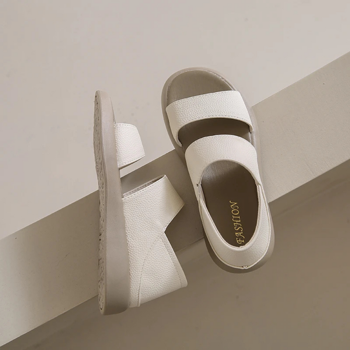 Weiße Sandalen mit zwei breiten Riemen auf beigem Hintergrund. Modische Sommerschuhe, bequem und stilvoll. Ideal für Damenmode und Freizeitkleidung.