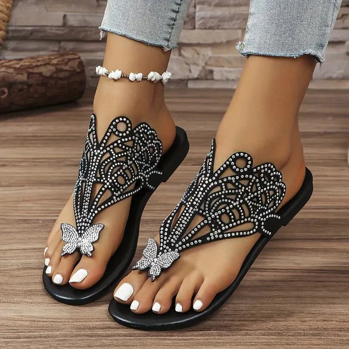 Damen Sandalen mit Strassverzierung und Schmetterlingsdesign, getragen mit Jeans und Fußkettchen. Elegante Sommerschuhe für Frauen.