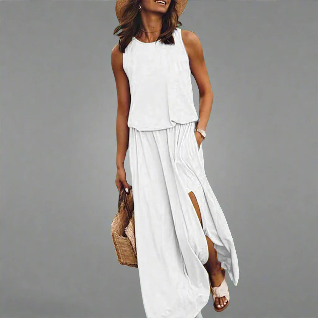 Frau in weißem Sommerkleid mit Schlitz, Strohhut und Sandalen, hält eine Strohtasche. Elegante Sommermode, lässiger Look.