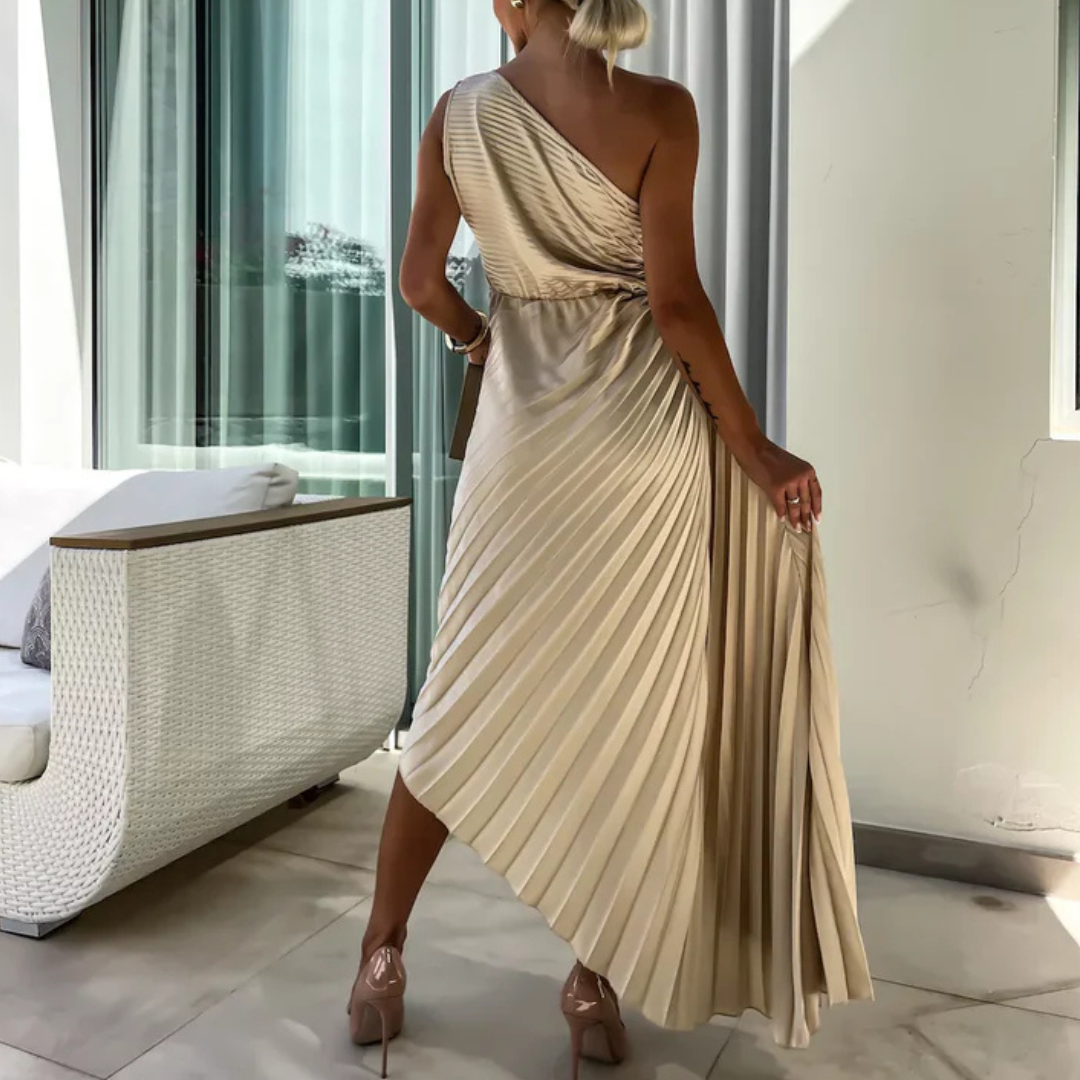 Frau in eleganter, einseitig schulterfreier, plissierter Abendkleid in Beige, steht auf Terrasse. Luxuriöse Mode, Sommerkleid, Abendgarderobe.