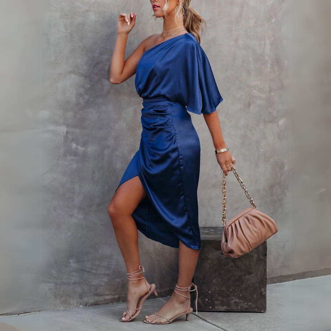 Elegantes blaues One-Shoulder-Kleid mit asymmetrischem Schnitt, kombiniert mit beigen High-Heels und einer beigen Handtasche. Perfekt für Abendmode.