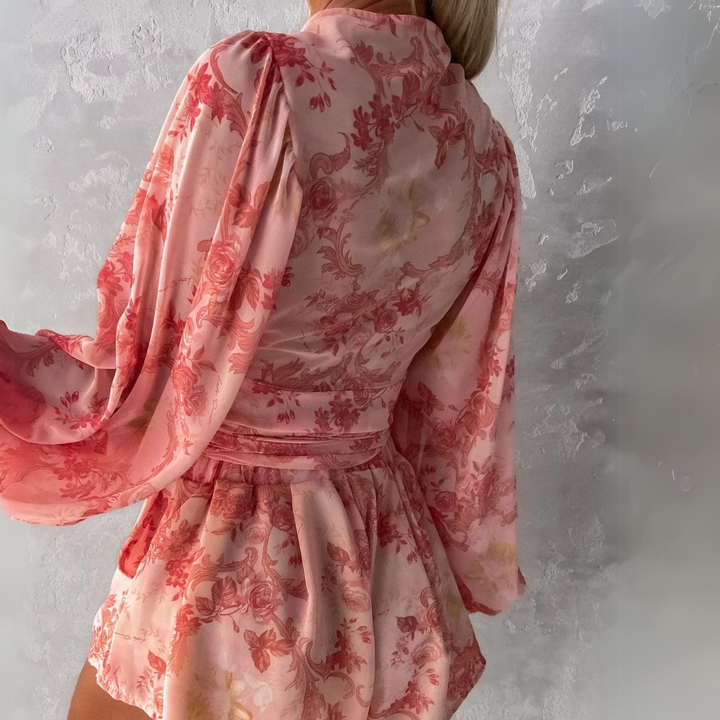 Frau in rosa geblümtem Kleid mit langen Ärmeln, Rückenansicht. Modetrend, elegantes Design, florales Muster, stilvolle Damenmode.