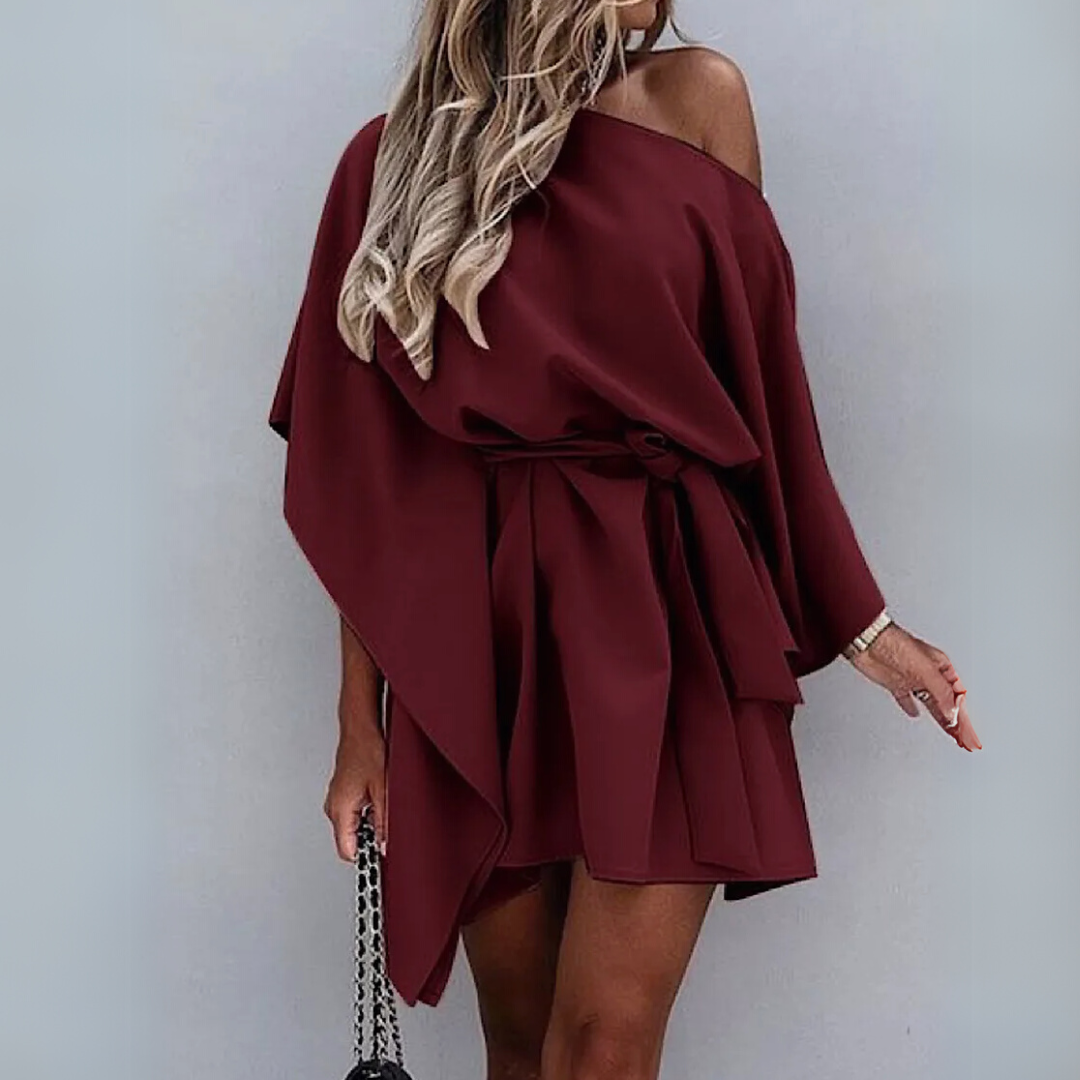 Frau in schulterfreiem, weinrotem Kleid mit Gürtel, hält schwarze Handtasche. Elegantes Outfit, modisches Design, trendige Damenmode.