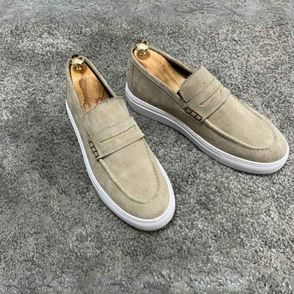 Beige Wildleder-Slipper mit weißer Sohle auf grauem Teppich. Modische Herrenschuhe, elegant und bequem, ideal für Freizeit und Büro.