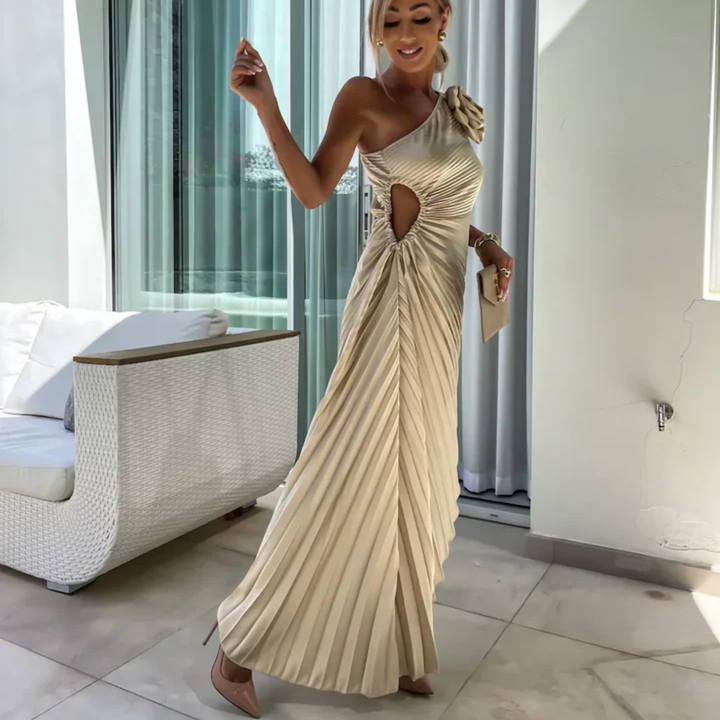 Elegantes, einseitiges, cremefarbenes Abendkleid mit Plisseefalten und Cut-Out-Detail, getragen von einer Frau in modernem, stilvollem Ambiente.