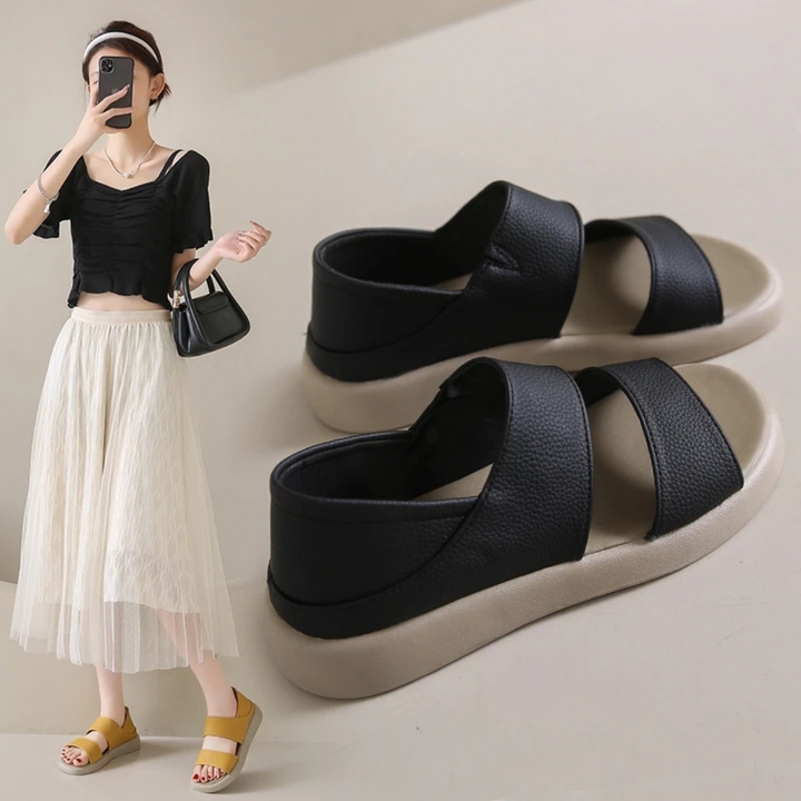 Damenmode: Schwarze Sandalen mit breiten Riemen und beiger Sohle, kombiniert mit schwarzem Top und weißem Rock. Sommeroutfit, stilvoll und bequem.