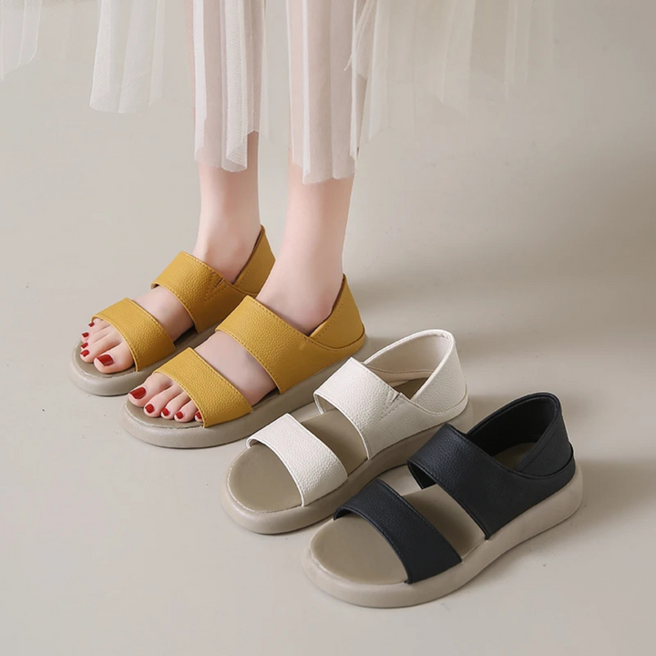 Damenfüße in weißen Sandalen neben gelben und schwarzen Sandalen auf hellem Boden. Modische Sommerschuhe, bequem und stilvoll.