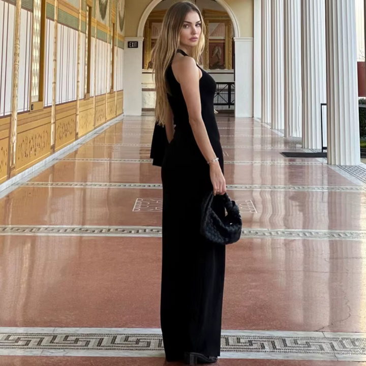 Frau in elegantem schwarzen Abendkleid steht in einem prunkvollen Korridor mit Säulen. Luxuriöse Mode, Abendgarderobe, stilvolle Architektur.