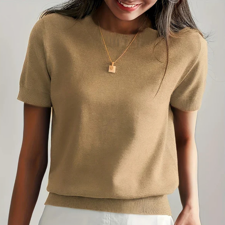 Frau trägt beigefarbenen Strickpullover und goldene Halskette, lächelt. Modetrend, Damenbekleidung, eleganter Freizeitlook.
