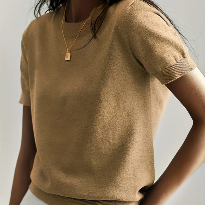 Frau in beigem T-Shirt mit kurzen Ärmeln und goldener Halskette. Modetrend, Damenbekleidung, minimalistischer Stil, elegantes Outfit.