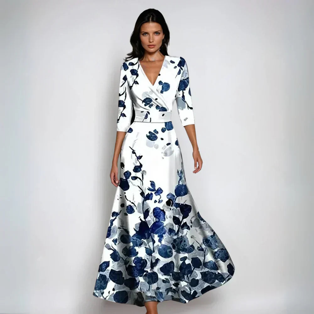 Frau in elegantem, langem Kleid mit blau-weißem Blumenmuster, V-Ausschnitt und Dreiviertelärmeln vor neutralem Hintergrund.