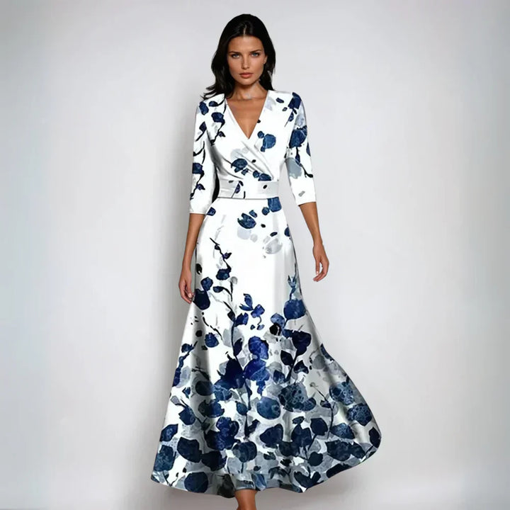 Frau in elegantem, langem Kleid mit blau-weißem Blumenmuster, V-Ausschnitt und Dreiviertelärmeln vor neutralem Hintergrund.
