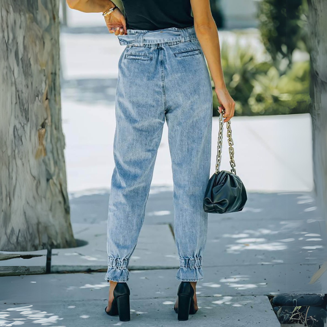 Frau in blauer High-Waist-Jeans und schwarzem Top, hält schwarze Handtasche mit Kettengriff. Modetrend, Streetstyle, Sommermode.