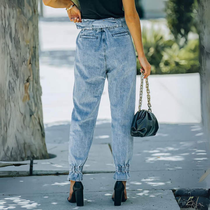 Frau in blauer High-Waist-Jeans und schwarzem Top, hält schwarze Handtasche mit Kettengriff. Modetrend, Streetstyle, Sommermode.