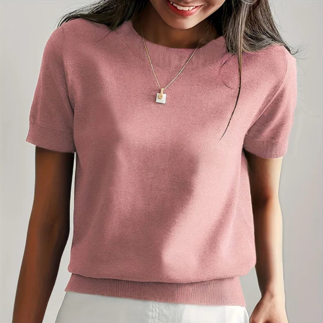 Frau trägt rosa Strickpullover und goldene Halskette, lächelt. Modetrend, Damenmode, eleganter Freizeitlook, stilvolles Outfit.