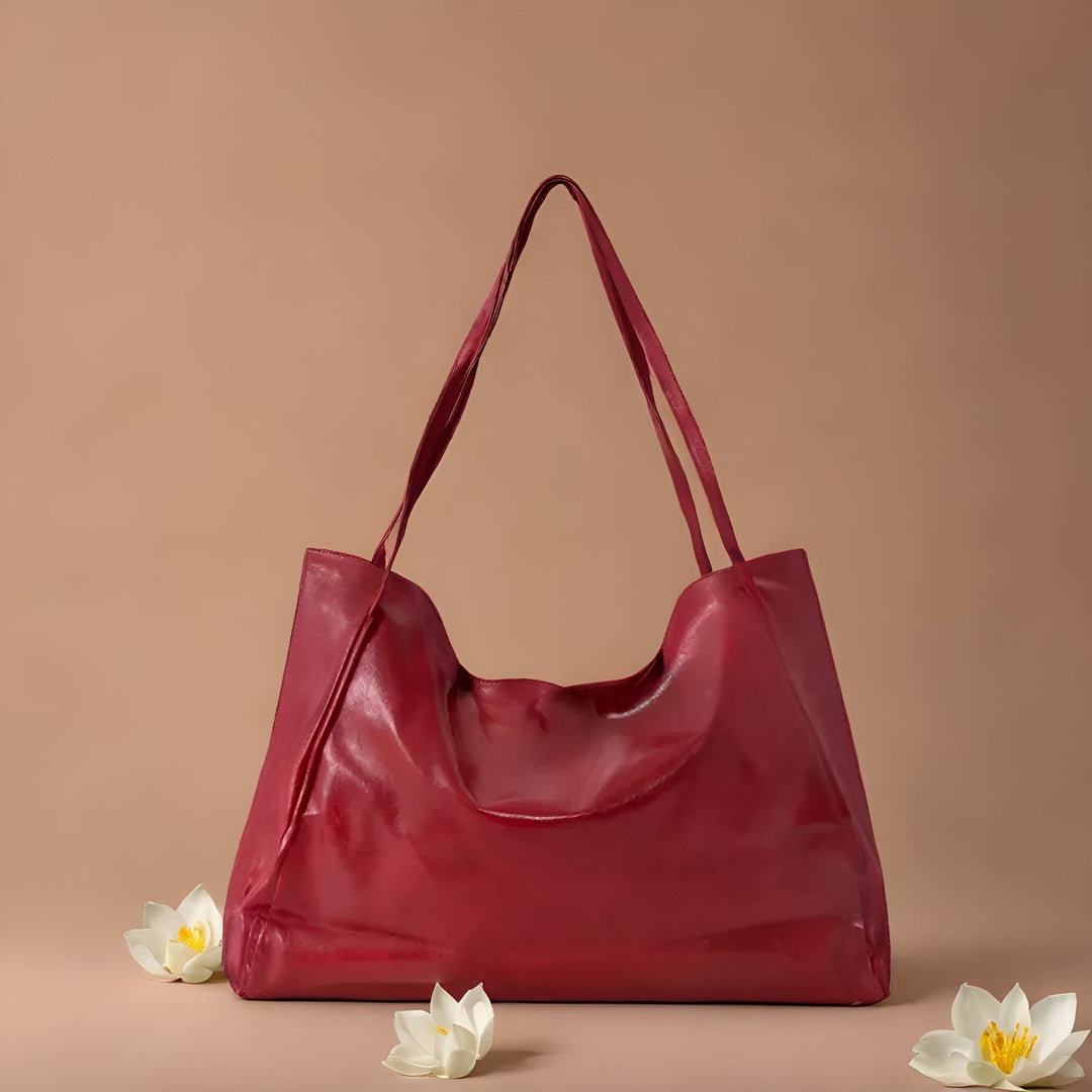 Rote Ledertasche mit langen Henkeln vor beigem Hintergrund, umgeben von weißen Lotusblüten. Elegante Damenhandtasche, modisches Accessoire.