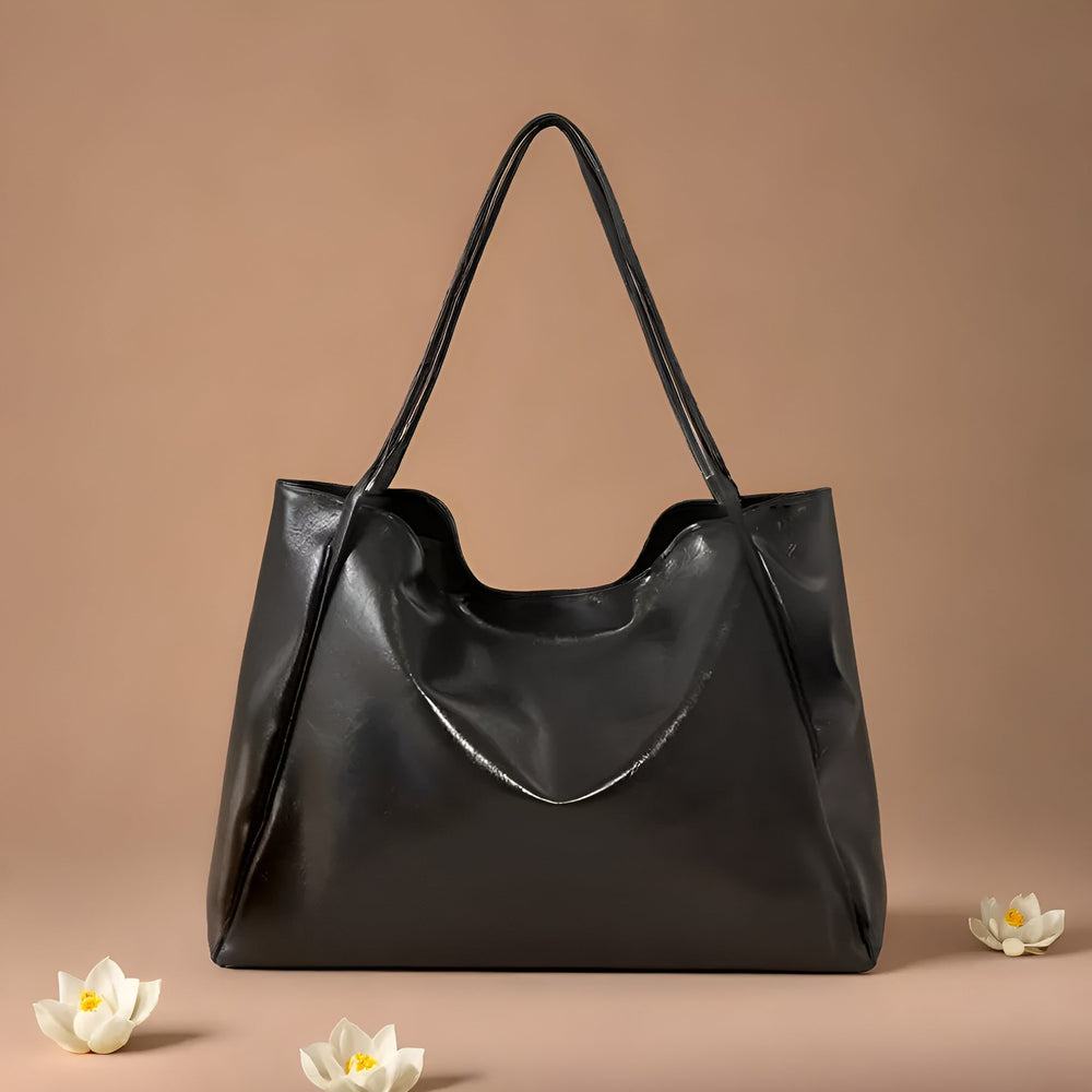 Schwarze Ledertasche mit langen Henkeln auf beigem Hintergrund, umgeben von weißen Lotusblüten. Elegante Damenhandtasche, modisches Accessoire.