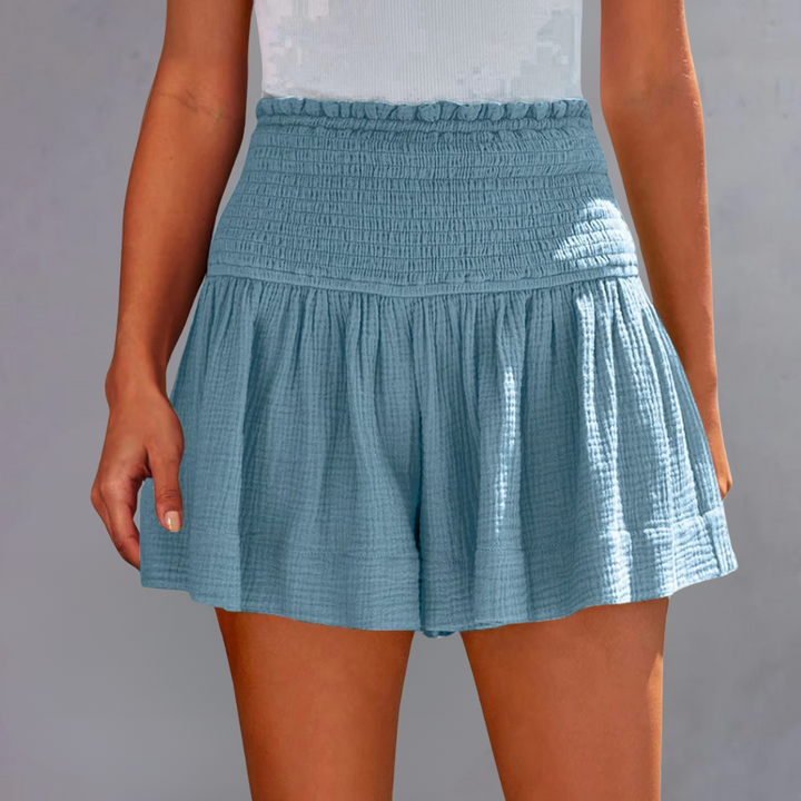 Frau trägt blaue, hoch taillierte Sommer-Shorts aus Baumwolle mit Rüschen. Ideal für Freizeitmode und Sommeroutfits.