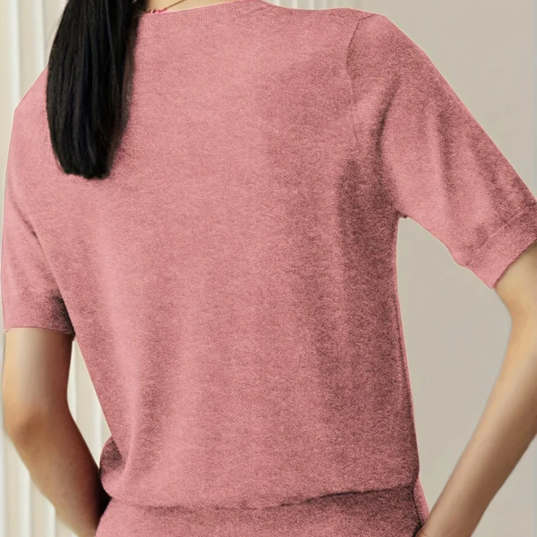 Rückansicht einer Frau in einem rosa T-Shirt, stehend vor einem neutralen Hintergrund. Modetrend, Damenbekleidung, Freizeitlook.