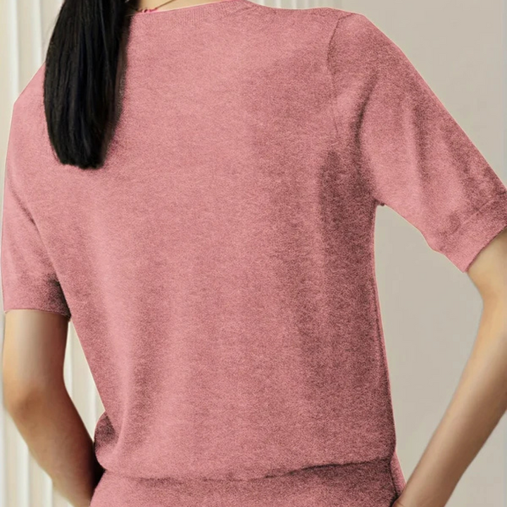 Rückansicht einer Frau in einem rosa T-Shirt, stehend vor einem neutralen Hintergrund. Modetrend, Damenbekleidung, Freizeitlook.