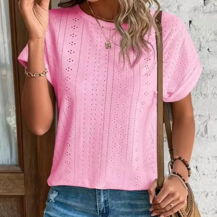 Frau in rosa Lochstickerei-T-Shirt und blauen Jeans vor weißer Wand. Modetrend, Sommeroutfit, Freizeitkleidung, Damenmode.