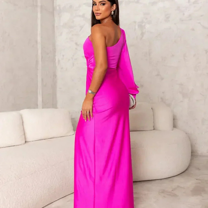 Eine Frau in einem leuchtend pinken, schulterfreien Abendkleid steht in einem modernen, minimalistischen Raum mit beiger Couch.