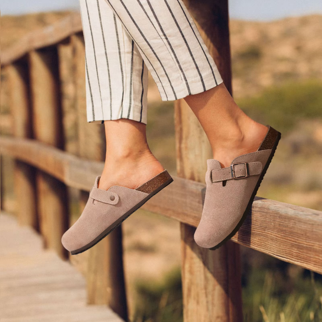 Damenfüße in beigen Clogs mit Schnalle auf Holzbrücke, gestreifte Hose, Sommermode, bequeme Schuhe, Outdoor, Freizeitlook.