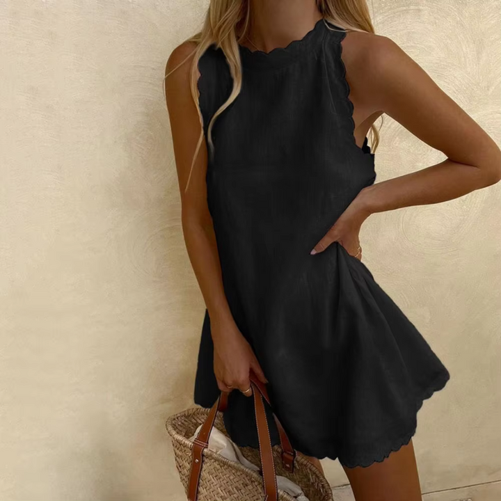 Blonde Frau in schwarzem Sommerkleid mit gewelltem Saum, hält einen geflochtenen Korb. Elegantes, lässiges Outfit für warme Tage.