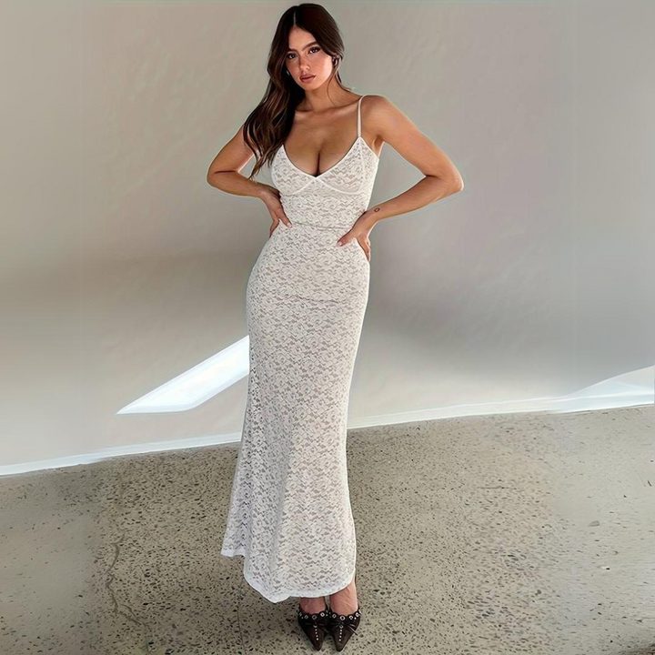 Frau in elegantem, weißem Spitzenkleid mit Spaghettiträgern, posiert auf Betonboden. Mode, Abendkleid, stilvoll, modern.