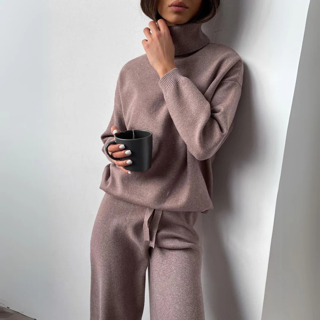 Frau in beigem Strickpullover und Hose hält schwarze Tasse. Modischer Herbst-Look, gemütlicher Rollkragenpullover, minimalistische Kleidung.