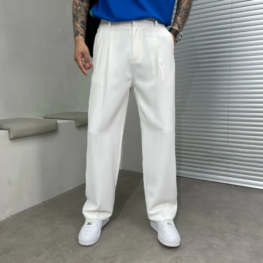 Mann in weißen Anzughosen und weißen Sneakers, steht vor grauer Wand. Moderne Herrenmode, eleganter Stil, Freizeitlook.