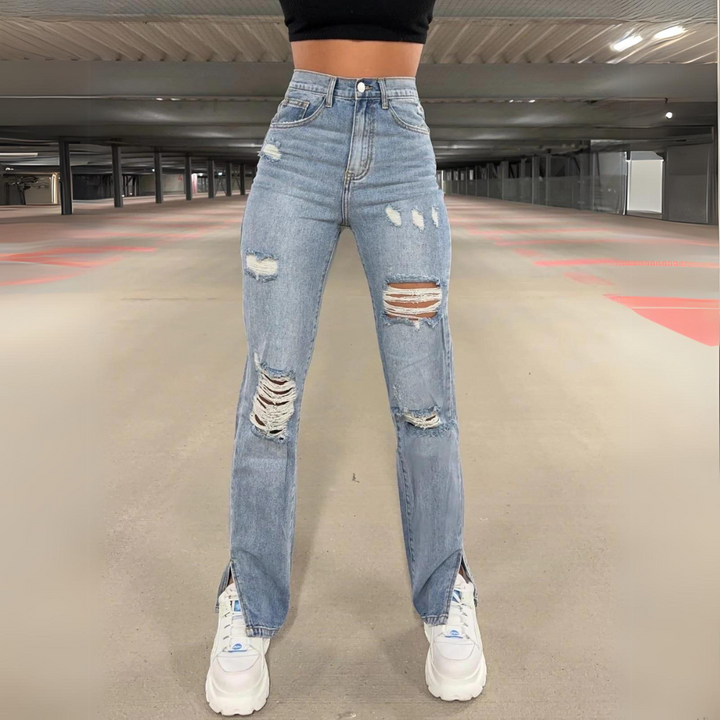 Frau in zerrissenen Jeans und weißen Sneakers in Parkhaus. Modetrend, Streetwear, lässiger Stil, hohe Taille, urbaner Look.