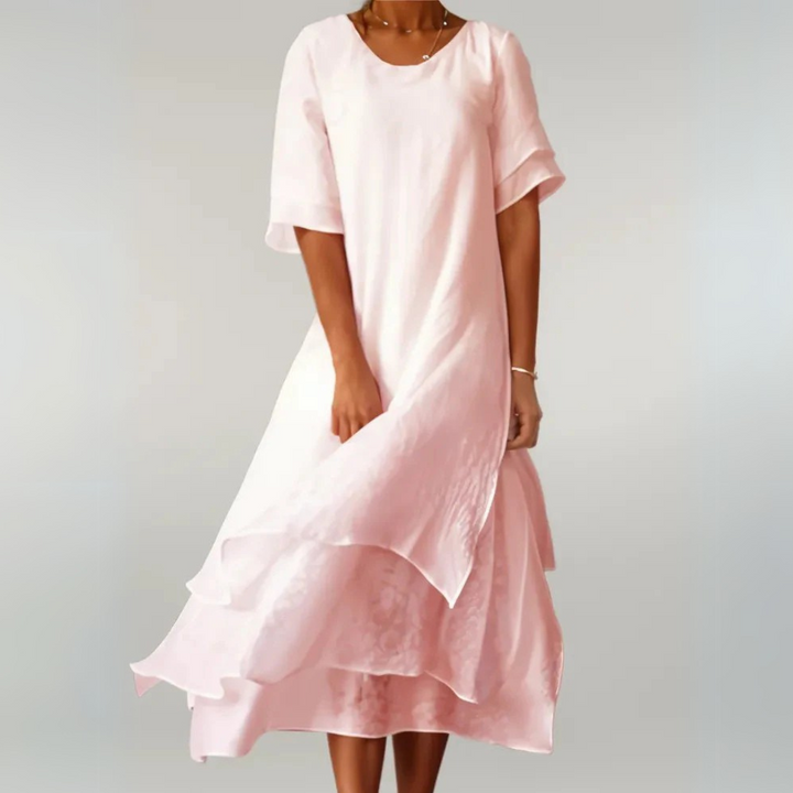 Dame in fließendem, rosa Sommerkleid mit asymmetrischem Saum vor grauem Hintergrund. Elegantes, luftiges Design für warme Tage.