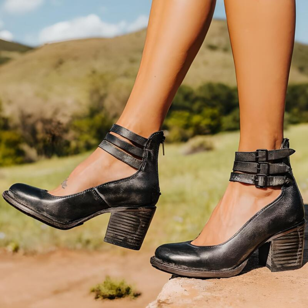 Schwarze Damenstiefeletten mit Blockabsatz und Schnallen, getragen im Freien vor einer grünen Landschaft. Modische Schuhe für Herbst und Frühling.