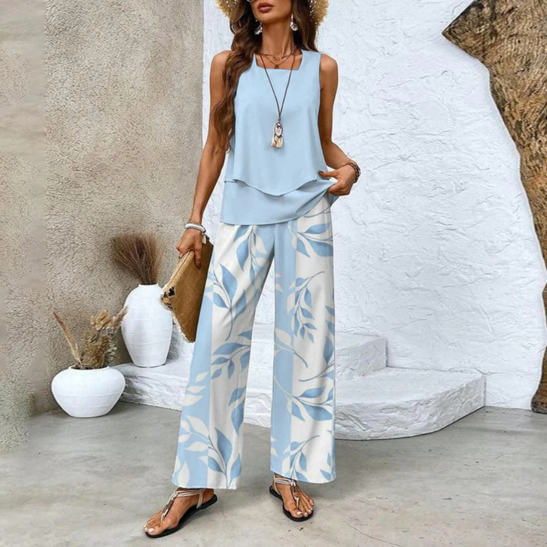 Frau in sommerlicher, hellblauer Bluse und weißer Hose mit Blattmuster, Strohhut und Sandalen. Elegante, lässige Mode für den Sommer.